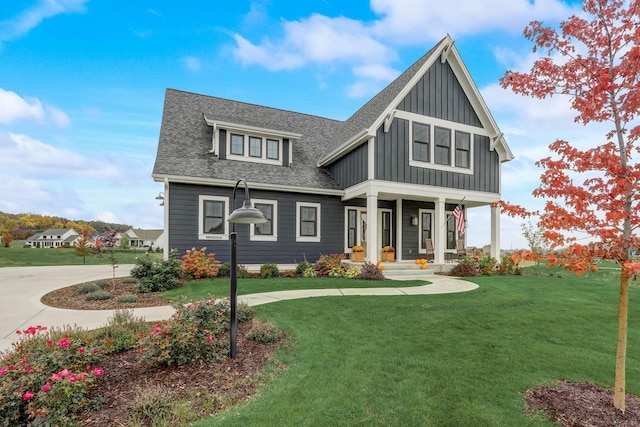 view of front of house featuring a front lawn, covered porch, board and batten siding, and roof with shingles