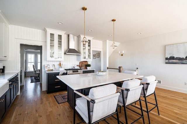 kitchen with wall chimney range hood, light countertops, a kitchen breakfast bar, light wood-style floors, and white cabinetry