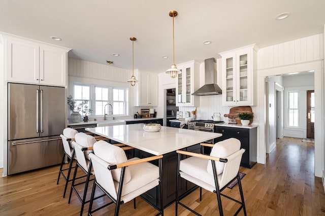 kitchen with a wealth of natural light, appliances with stainless steel finishes, wall chimney exhaust hood, and white cabinets