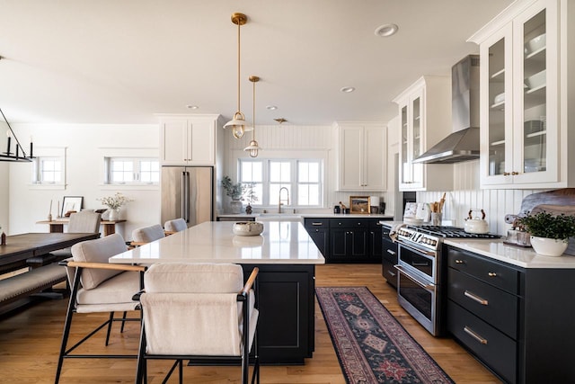 kitchen featuring white cabinets, appliances with stainless steel finishes, wall chimney range hood, and dark cabinets