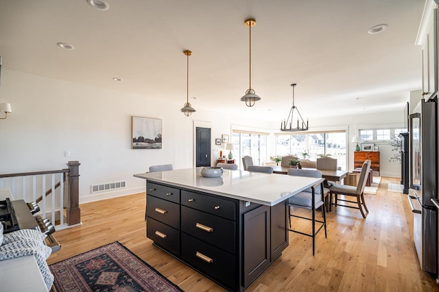 kitchen with visible vents, a kitchen bar, dark cabinetry, and light wood-style flooring