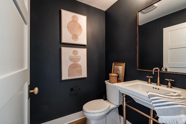 half bath with visible vents, toilet, baseboards, and a sink