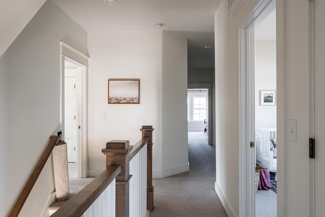 hall with an upstairs landing, baseboards, and carpet floors