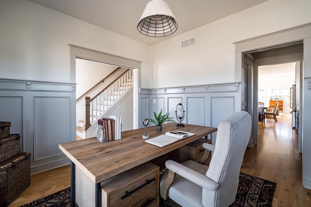 dining area with visible vents, hardwood / wood-style floors, stairway, wainscoting, and a decorative wall