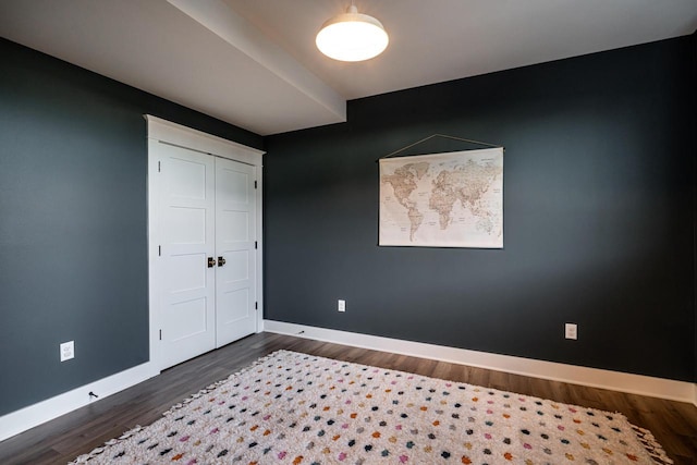 unfurnished bedroom with a closet, baseboards, and dark wood-style floors