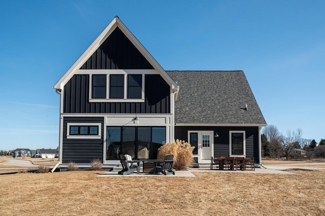 rear view of property with a lawn, board and batten siding, a shingled roof, and a patio