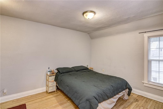 bedroom featuring a textured ceiling, light wood finished floors, lofted ceiling, and baseboards