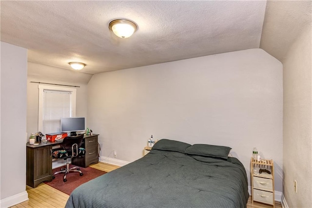 bedroom featuring lofted ceiling, light wood-style flooring, baseboards, and a textured ceiling