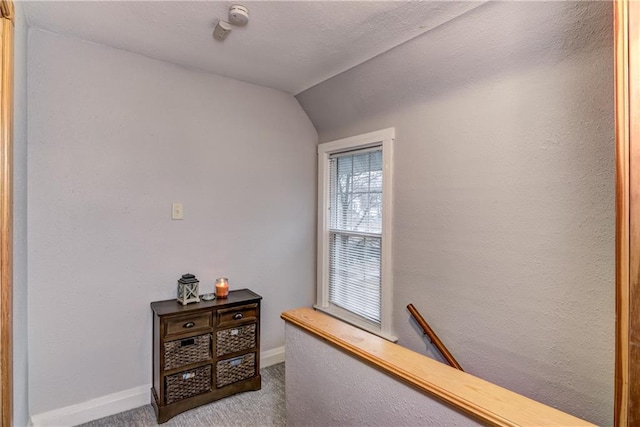 hall featuring lofted ceiling, baseboards, carpet flooring, and a textured wall