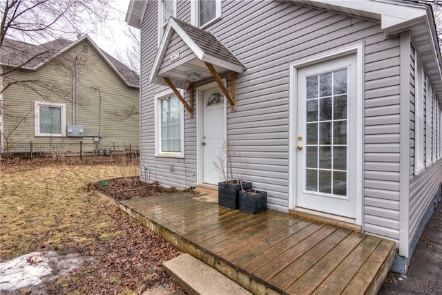 doorway to property featuring roof with shingles, fence, and a deck