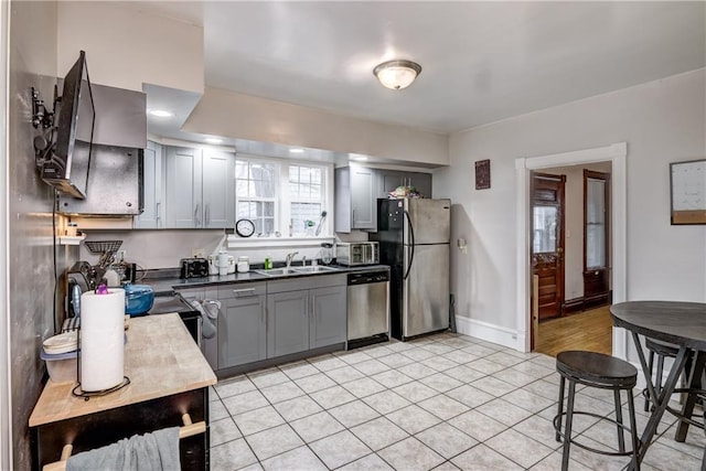 kitchen with dark countertops, gray cabinets, stainless steel appliances, and a sink