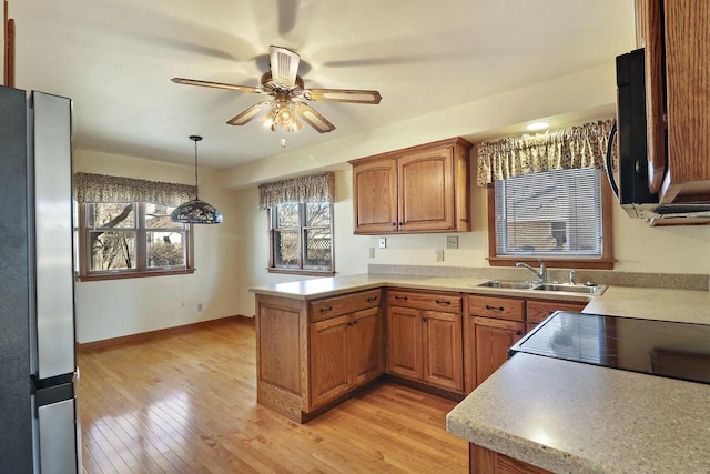 kitchen with brown cabinets, a peninsula, light countertops, light wood-style floors, and a sink