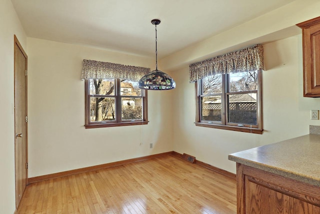 unfurnished dining area with light wood-type flooring, a healthy amount of sunlight, and baseboards