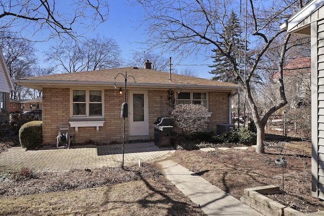 view of front of home with a patio, brick siding, a chimney, and roof with shingles