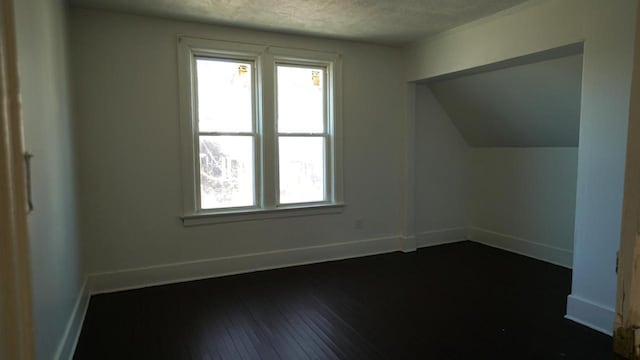 bonus room with a healthy amount of sunlight, dark wood finished floors, a textured ceiling, and baseboards