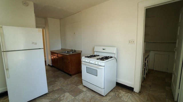 kitchen featuring stone finish flooring, white appliances, a sink, and baseboards