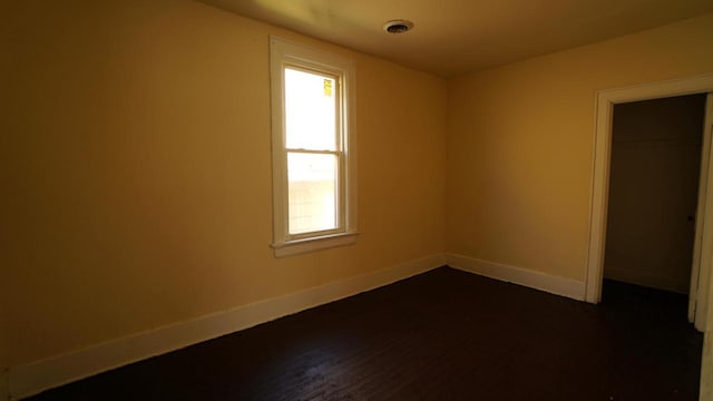 spare room with dark wood-style floors, visible vents, and baseboards