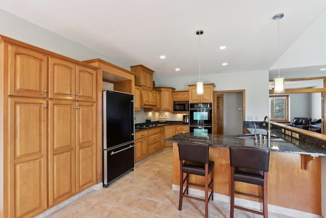 kitchen with a kitchen bar, black appliances, a sink, decorative light fixtures, and dark stone countertops