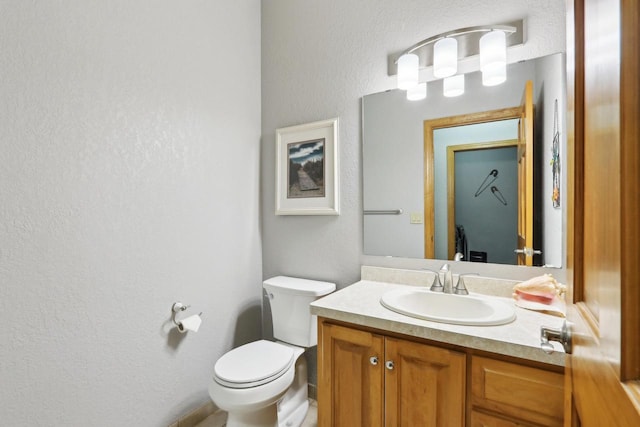 bathroom featuring toilet, vanity, and a textured wall