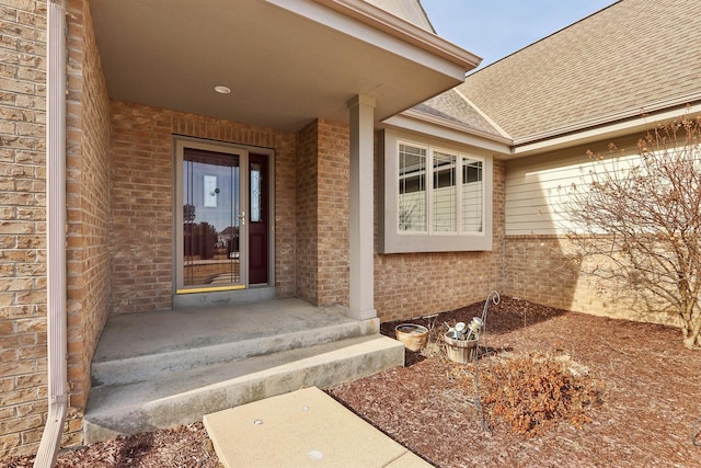 view of exterior entry with brick siding and roof with shingles