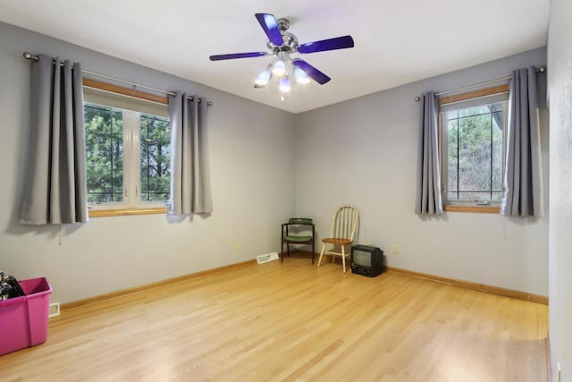 living area with visible vents, baseboards, wood finished floors, and a ceiling fan