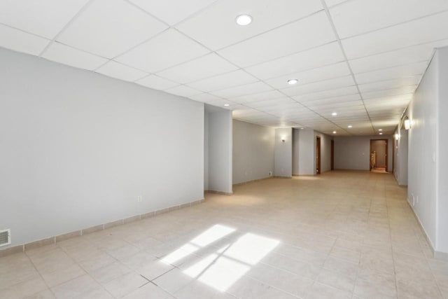 finished below grade area featuring light tile patterned floors, visible vents, a paneled ceiling, and baseboards