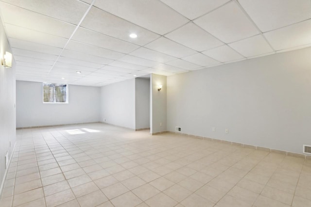 basement featuring light tile patterned flooring, baseboards, visible vents, and a drop ceiling