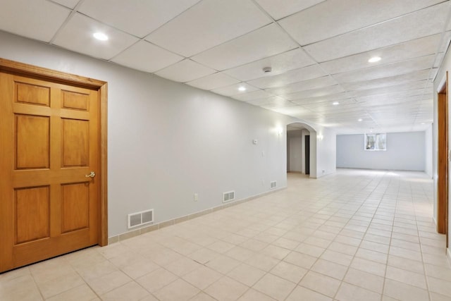 basement featuring arched walkways, visible vents, and a drop ceiling