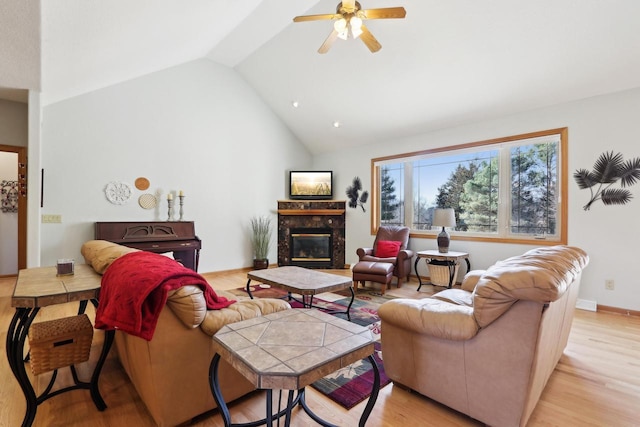 living room featuring baseboards, light wood finished floors, high vaulted ceiling, a high end fireplace, and ceiling fan