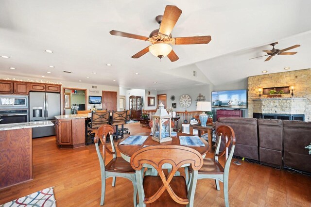 dining room with a ceiling fan, recessed lighting, a fireplace, light wood finished floors, and vaulted ceiling