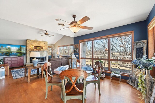 dining space featuring visible vents, ceiling fan, vaulted ceiling, a fireplace, and wood finished floors