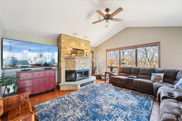 living room featuring a stone fireplace, lofted ceiling, wood finished floors, and a ceiling fan