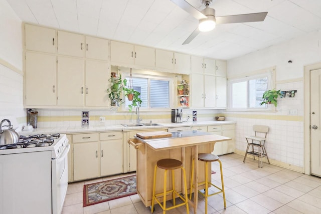 kitchen with a ceiling fan, a sink, light countertops, light tile patterned floors, and white range with gas stovetop