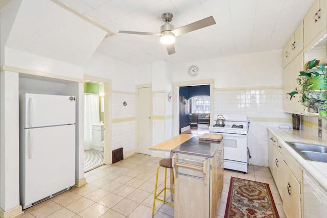 kitchen with a sink, white appliances, tile walls, light tile patterned flooring, and light countertops