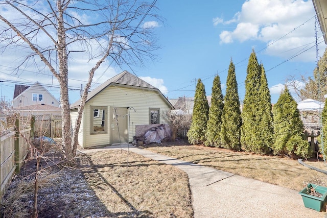 rear view of property featuring an outdoor structure and fence