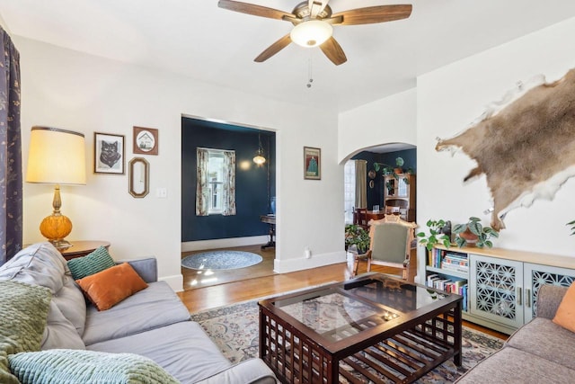 living room with arched walkways, ceiling fan, baseboards, and wood finished floors