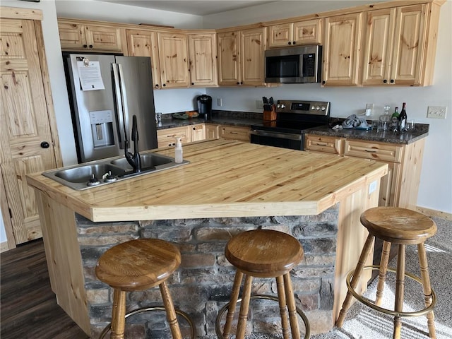 kitchen with wooden counters, light brown cabinetry, appliances with stainless steel finishes, a kitchen breakfast bar, and a sink