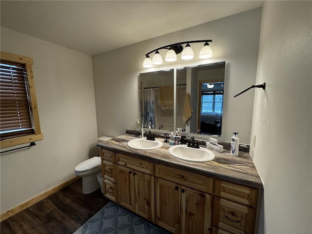 full bath with double vanity, toilet, wood finished floors, and a sink