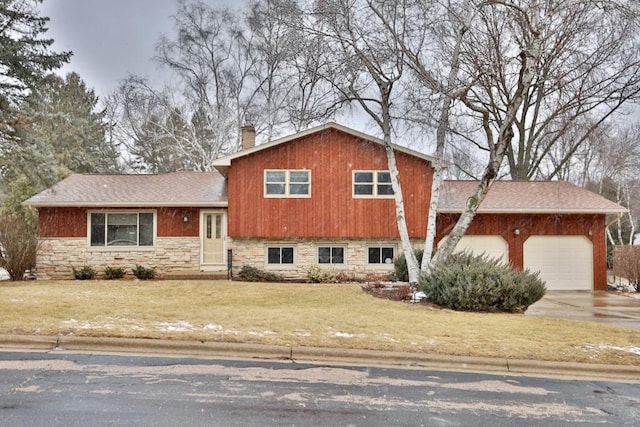 tri-level home featuring a garage, stone siding, concrete driveway, a chimney, and a front yard