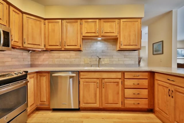 kitchen with stainless steel appliances, tasteful backsplash, light wood-type flooring, and a sink