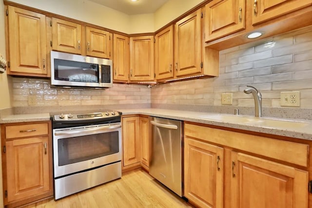 kitchen featuring light wood-style floors, light stone counters, stainless steel appliances, and a sink