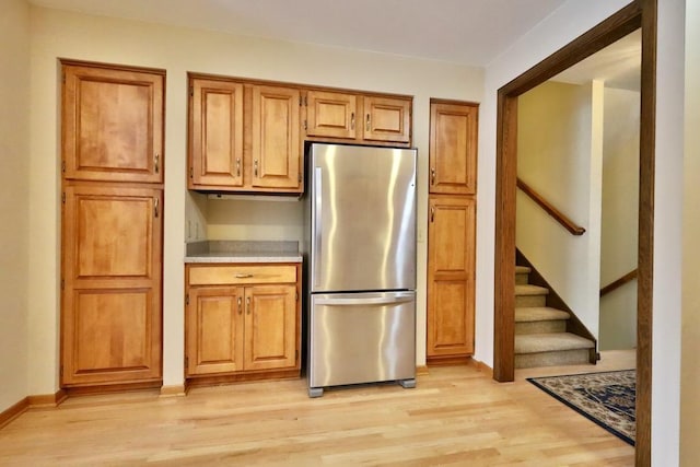 kitchen with light countertops, light wood-type flooring, freestanding refrigerator, and brown cabinets