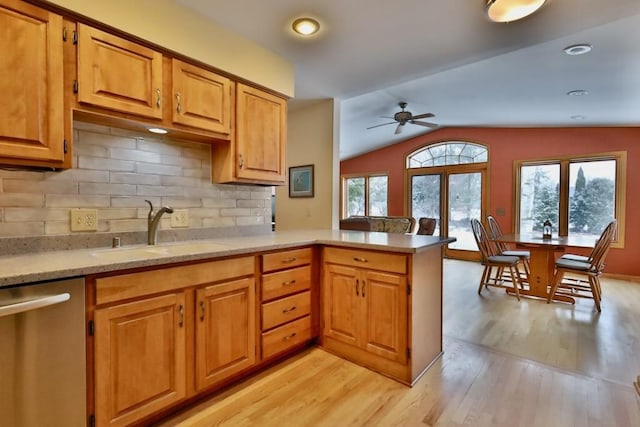 kitchen featuring lofted ceiling, a peninsula, light wood-type flooring, stainless steel dishwasher, and a sink