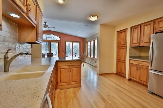 kitchen with freestanding refrigerator, a peninsula, baseboard heating, light wood-type flooring, and a sink