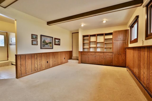 unfurnished living room with a wainscoted wall, light carpet, beam ceiling, and wooden walls