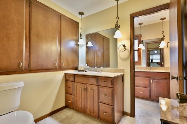 bathroom featuring baseboards, two vanities, a sink, and toilet