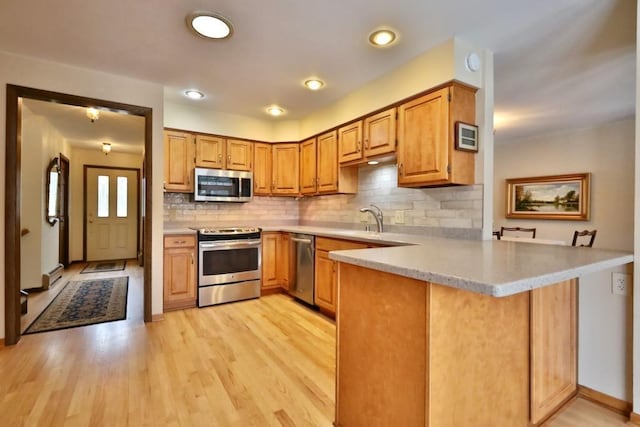 kitchen featuring stainless steel appliances, light countertops, backsplash, light wood-style floors, and a peninsula