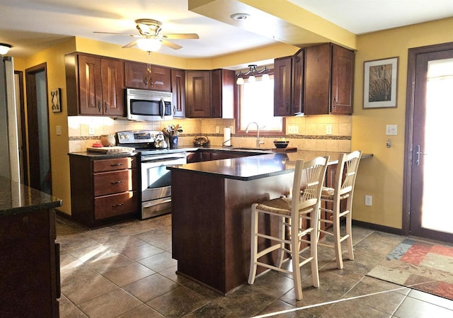 kitchen with tasteful backsplash, dark countertops, a kitchen breakfast bar, stainless steel appliances, and a sink