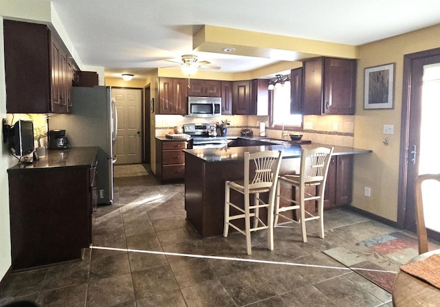 kitchen with a sink, dark brown cabinets, appliances with stainless steel finishes, dark countertops, and a kitchen bar