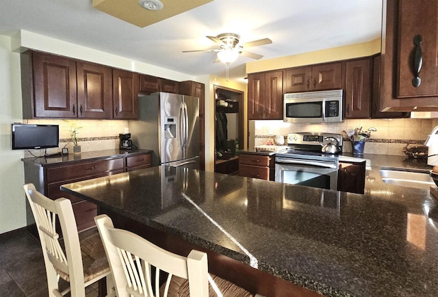 kitchen featuring a breakfast bar area, stainless steel appliances, backsplash, a sink, and dark stone counters